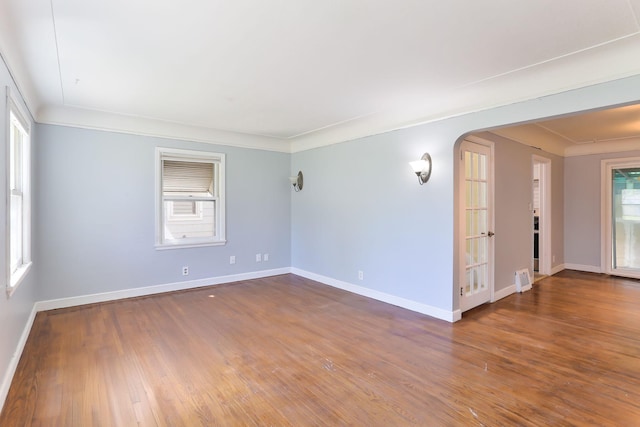 empty room with arched walkways, wood finished floors, baseboards, and ornamental molding