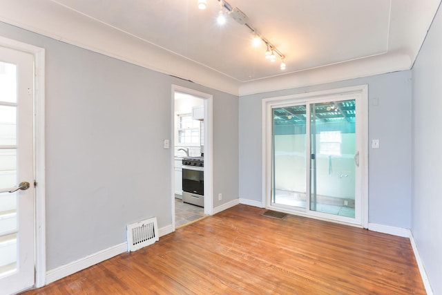 spare room featuring rail lighting, baseboards, light wood-style floors, and a sink
