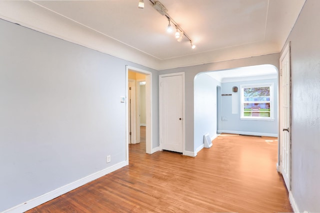 spare room featuring arched walkways, light wood-style floors, track lighting, and baseboards