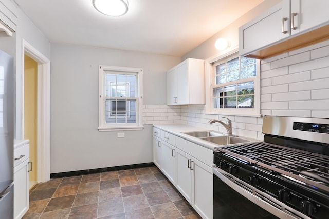 kitchen featuring gas range, a sink, tasteful backsplash, baseboards, and dark stone finish flooring