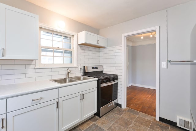 kitchen with gas stove, a sink, decorative backsplash, white cabinets, and stone finish flooring