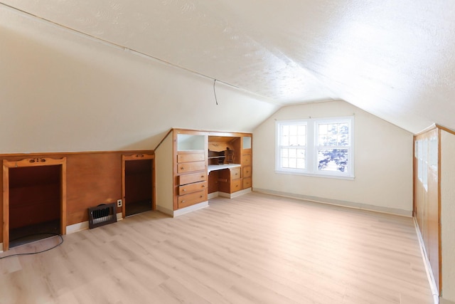 bonus room with light wood-style flooring, vaulted ceiling, baseboards, and a textured ceiling