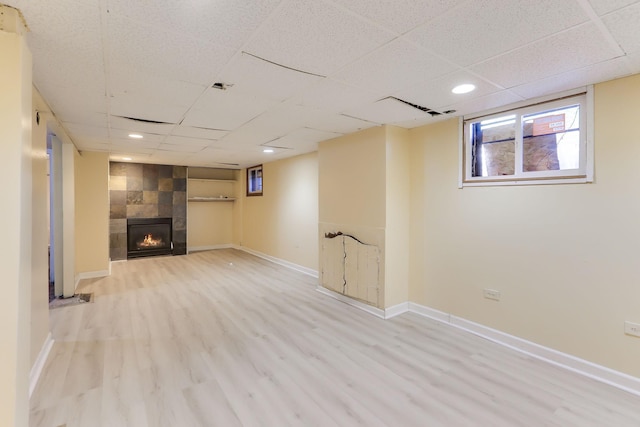 basement featuring a tiled fireplace, wood finished floors, baseboards, and a drop ceiling