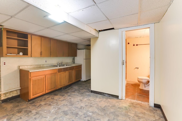 kitchen featuring freestanding refrigerator, a paneled ceiling, light countertops, a sink, and baseboards