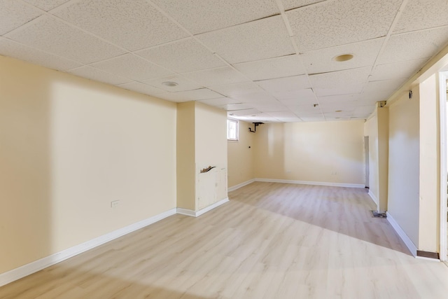 below grade area featuring light wood-style floors, a paneled ceiling, and baseboards