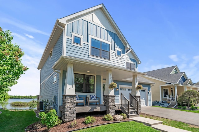 craftsman house featuring covered porch, board and batten siding, a water view, a front yard, and asphalt driveway