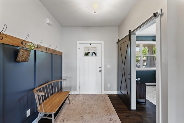 foyer entrance featuring a barn door, dark wood-type flooring, and baseboards