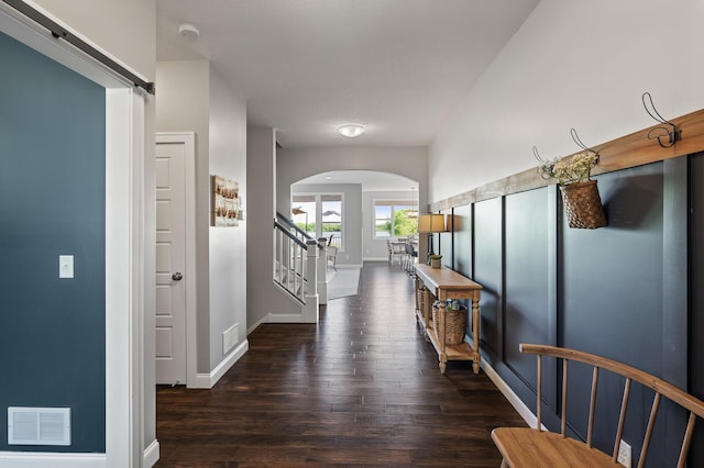 hall with arched walkways, wood finished floors, baseboards, and stairway