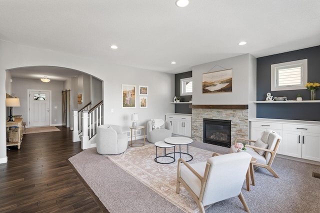 living area with arched walkways, recessed lighting, dark wood-style flooring, stairs, and a stone fireplace
