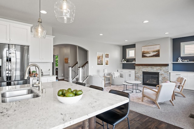 kitchen with stainless steel fridge, a sink, a stone fireplace, recessed lighting, and dark wood-style floors