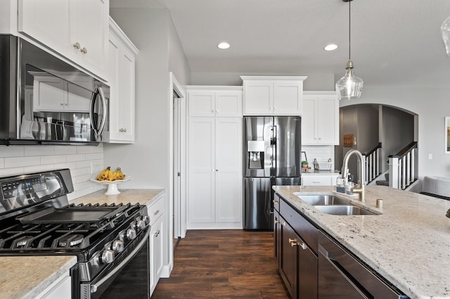 kitchen with stainless steel appliances, a sink, arched walkways, white cabinetry, and recessed lighting