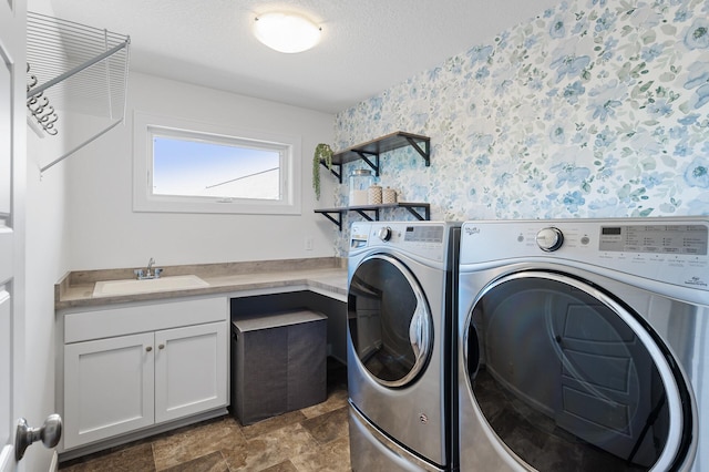 laundry room featuring wallpapered walls, washing machine and clothes dryer, a textured ceiling, cabinet space, and stone finish floors