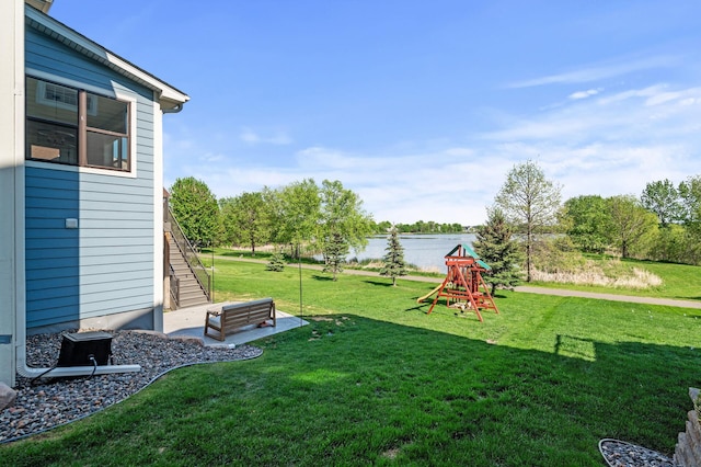 view of grassy yard featuring a water view, a playground, and stairway