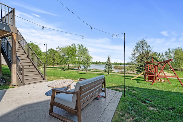 view of grassy yard with stairway, a playground, a patio, and a water view