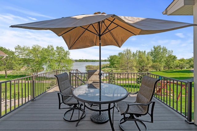 wooden deck with a water view, outdoor dining space, and a yard