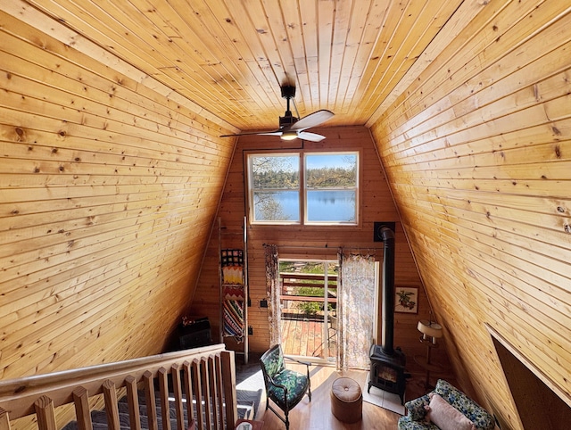 living area featuring a wood stove, wood ceiling, wooden walls, ceiling fan, and a water view