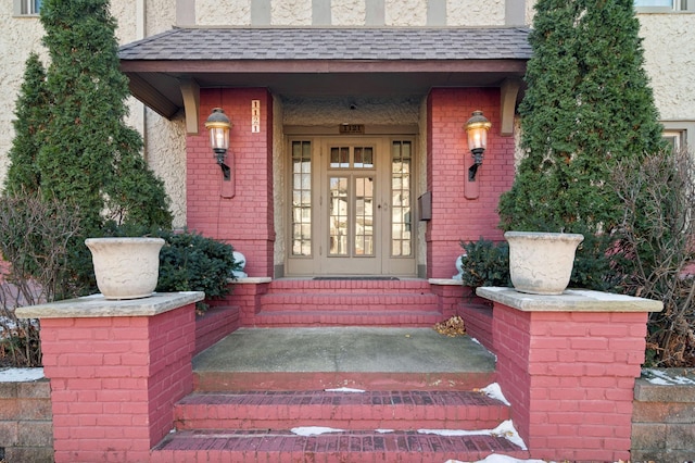 entrance to property with brick siding, covered porch, and a shingled roof
