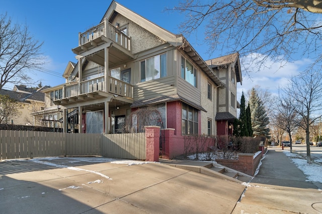 view of side of home featuring a balcony, fence, and brick siding