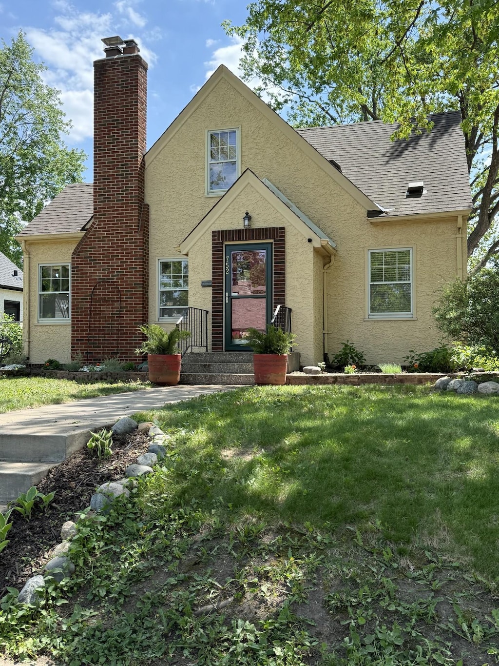 view of front of property featuring stucco siding, a front yard, a chimney, and roof with shingles