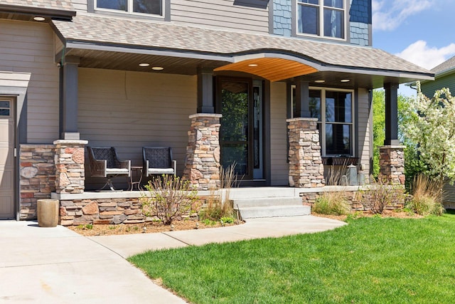 view of exterior entry featuring stone siding, a yard, a shingled roof, and a porch