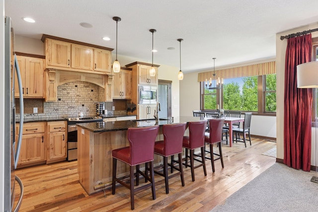 kitchen featuring stainless steel appliances, a kitchen island with sink, light wood-style floors, a sink, and backsplash