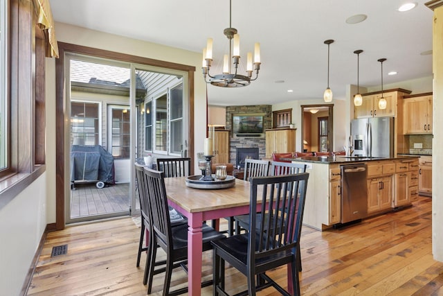 dining area featuring light wood finished floors, a chandelier, recessed lighting, a stone fireplace, and baseboards