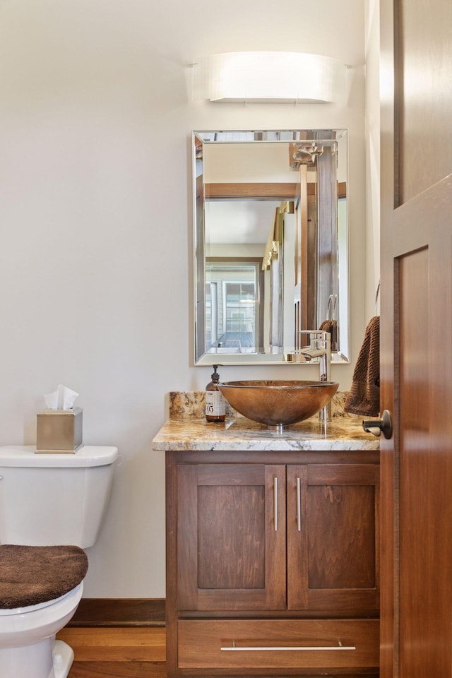 half bath featuring toilet, baseboards, wood finished floors, and vanity