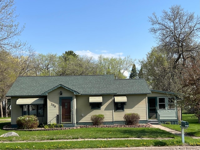 view of front of house featuring entry steps, a front lawn, and a shingled roof