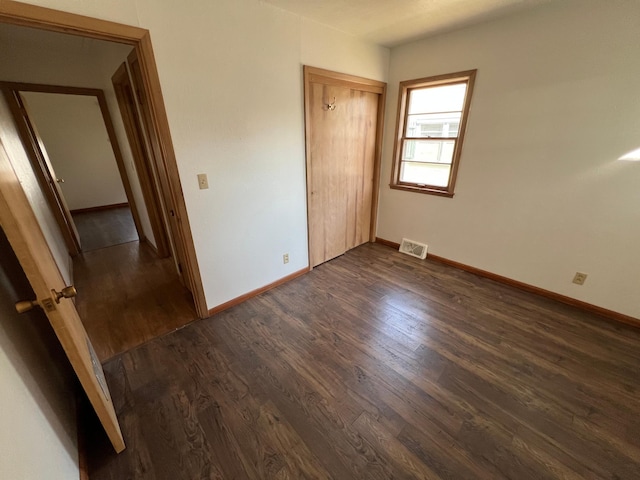unfurnished bedroom featuring dark wood-type flooring, baseboards, and a closet