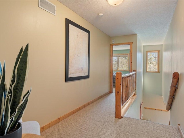 hall with carpet, an upstairs landing, a textured ceiling, and baseboards