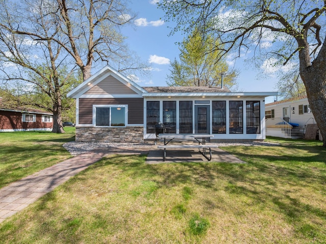 rear view of property featuring a sunroom, a lawn, stone siding, and a patio area