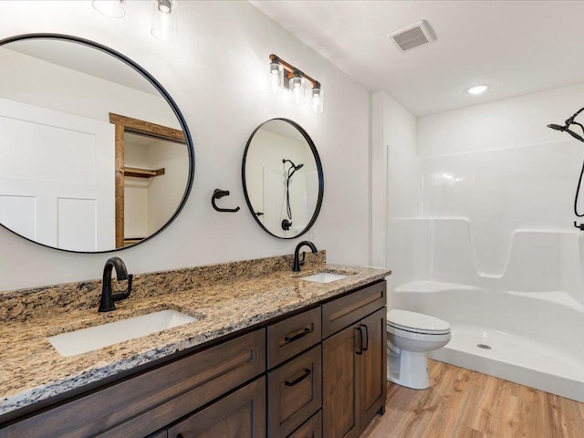 full bath with wood finished floors, a shower, double vanity, and toilet