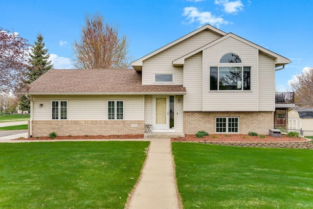 split level home featuring brick siding, a front yard, a storage shed, and an outdoor structure
