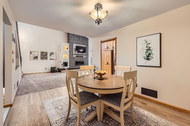 58 Garden Dr, Burnsville, MN 55337 - dining area with a fireplace, light wood-style flooring, a textured ceiling, and baseboards
