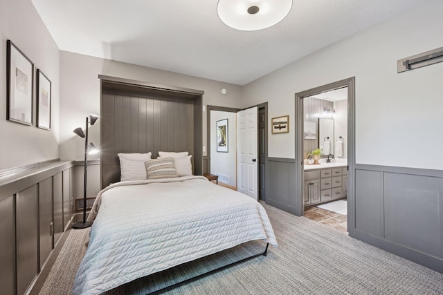 19820 Schutte Farm Rd, Corcoran, MN 55340 - bedroom featuring light carpet, a sink, connected bathroom, wainscoting, and a decorative wall