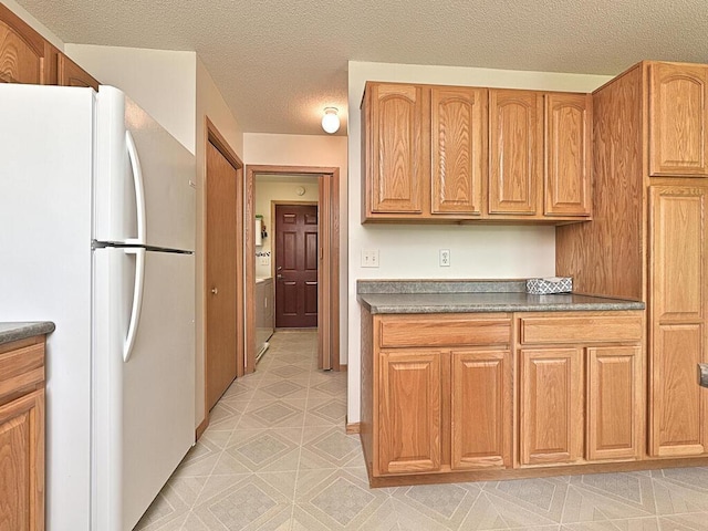 38850 Christie Ln, Cohasset, MN 55721 - kitchen featuring freestanding refrigerator, dark countertops, a textured ceiling, washer / dryer, and brown cabinetry