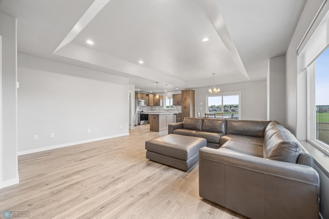 living area featuring a chandelier, light wood-style flooring, baseboards, recessed lighting, and a tray ceiling