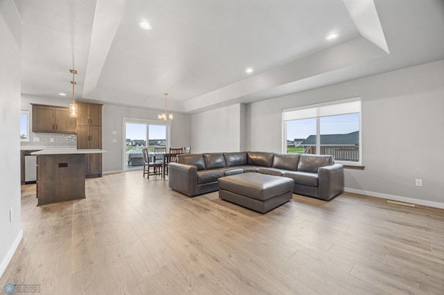 living area featuring a tray ceiling, light wood-style floors, a chandelier, baseboards, and recessed lighting