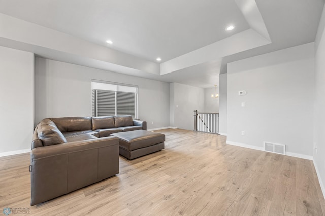 living room with a tray ceiling, light wood-type flooring, baseboards, and recessed lighting