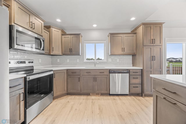 kitchen featuring appliances with stainless steel finishes, a sink, decorative backsplash, light wood-style floors, and recessed lighting