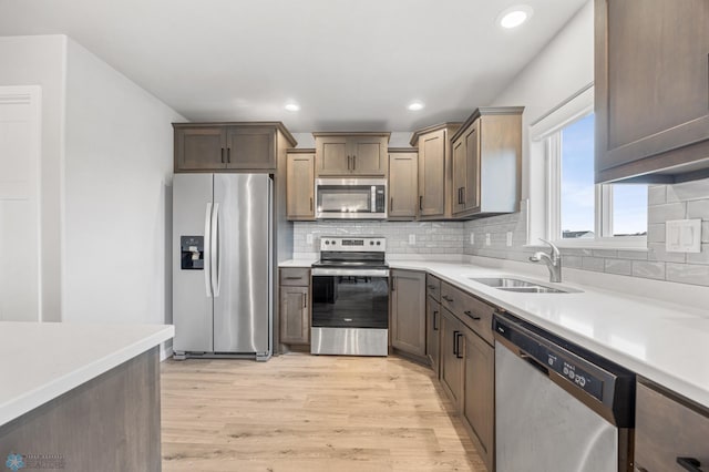 kitchen with appliances with stainless steel finishes, light wood finished floors, a sink, light countertops, and decorative backsplash