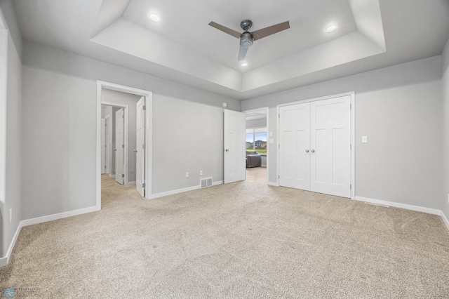 unfurnished bedroom featuring a tray ceiling, carpet, recessed lighting, baseboards, and ceiling fan