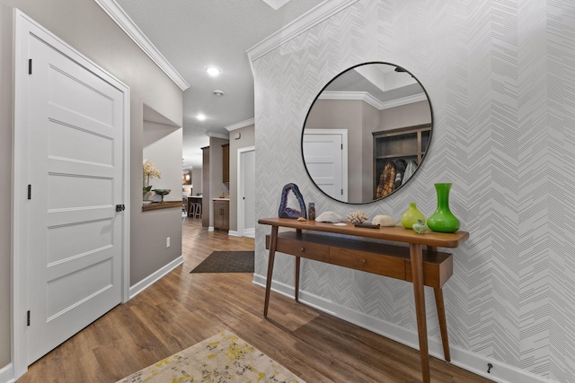 corridor featuring wallpapered walls, crown molding, baseboards, wood finished floors, and an accent wall