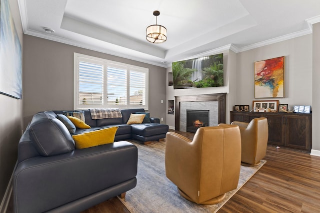 living area with a tray ceiling, a fireplace, wood finished floors, and ornamental molding
