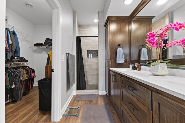 full bathroom featuring a stall shower, wood finished floors, vanity, a walk in closet, and baseboards