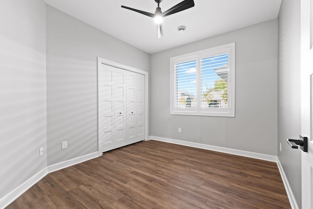 unfurnished bedroom featuring dark wood-type flooring, baseboards, a ceiling fan, and a closet