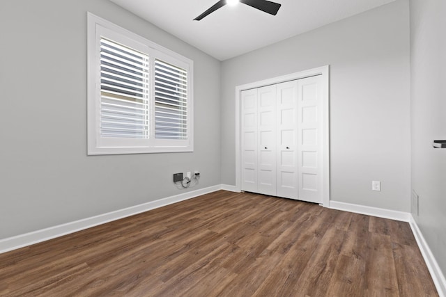 unfurnished bedroom featuring dark wood-style floors, baseboards, a closet, and a ceiling fan