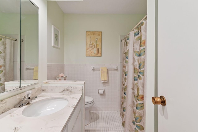 bathroom with tile patterned flooring, tile walls, vanity, toilet, and wainscoting