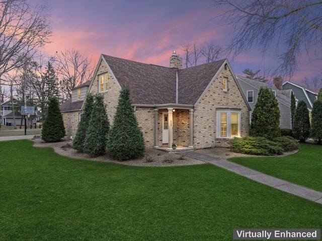 english style home featuring a lawn, brick siding, and a chimney