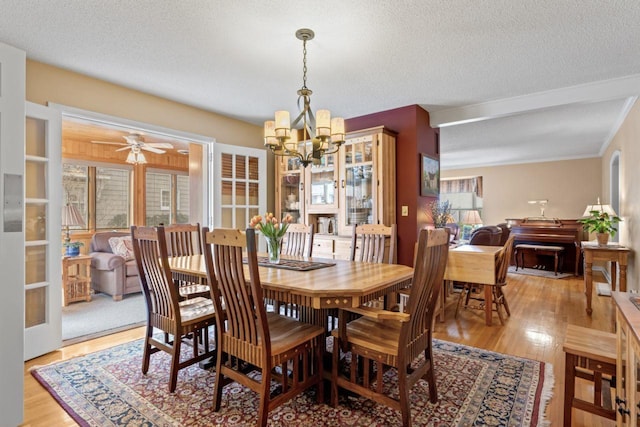 dining room featuring a chandelier, light wood-style floors, a textured ceiling, a ceiling fan, and ornamental molding